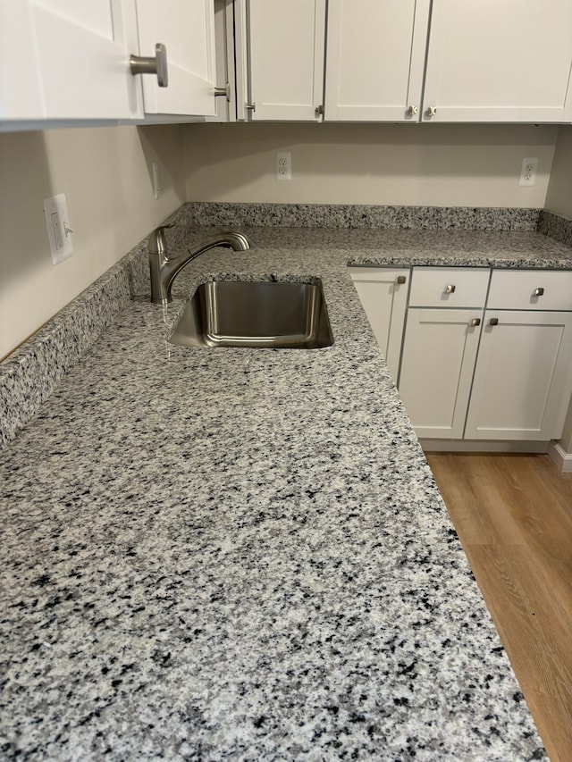 room details with white cabinets, light hardwood / wood-style floors, light stone counters, and sink