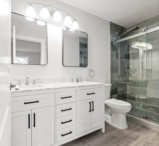 bathroom with hardwood / wood-style floors, vanity, toilet, and a shower with shower door