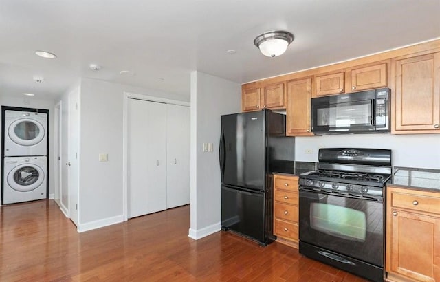 kitchen featuring black appliances, dark hardwood / wood-style floors, and stacked washer and dryer