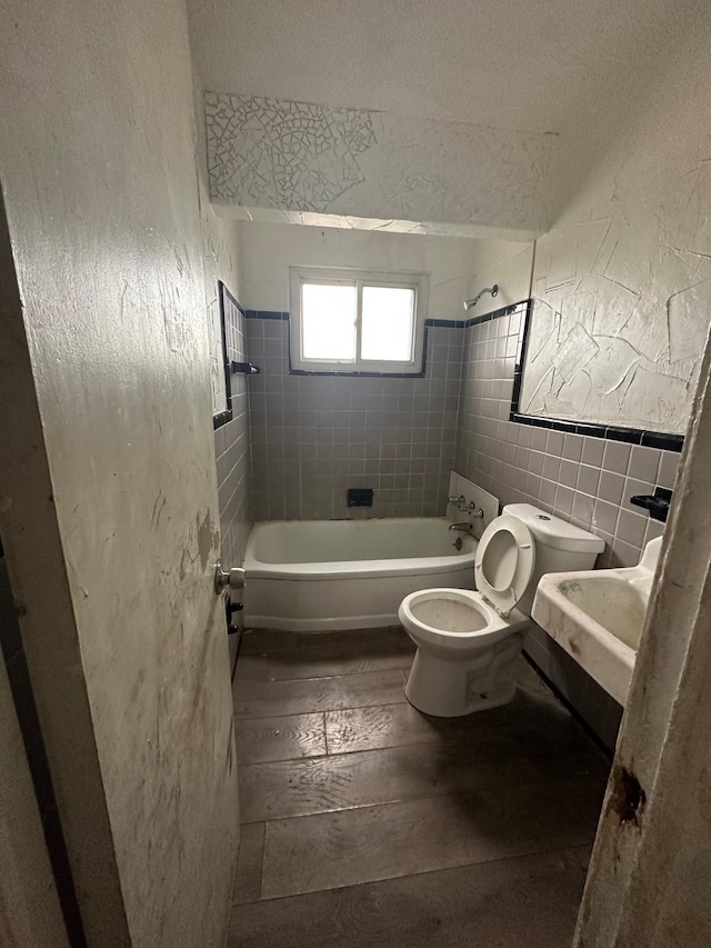 full bathroom with hardwood / wood-style flooring, tiled shower / bath combo, toilet, tile walls, and a textured ceiling