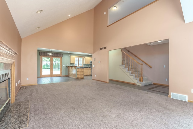 unfurnished living room with light carpet, a high end fireplace, high vaulted ceiling, and french doors