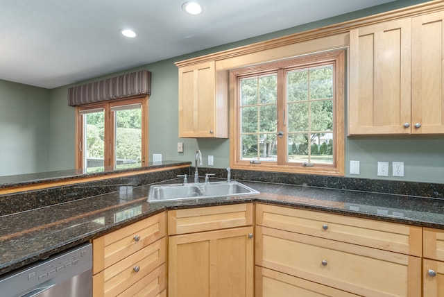 kitchen featuring dishwasher, sink, light brown cabinetry, and dark stone counters