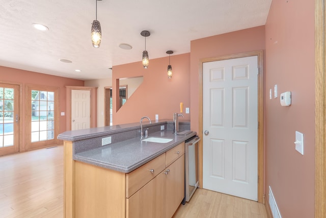 kitchen featuring pendant lighting, light brown cabinetry, sink, stainless steel dishwasher, and light hardwood / wood-style floors