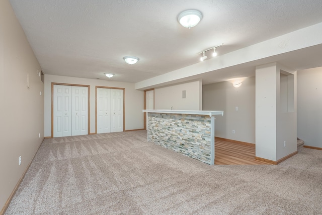 basement with track lighting, light carpet, and a textured ceiling