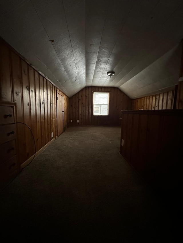 additional living space featuring dark colored carpet, wooden walls, and vaulted ceiling