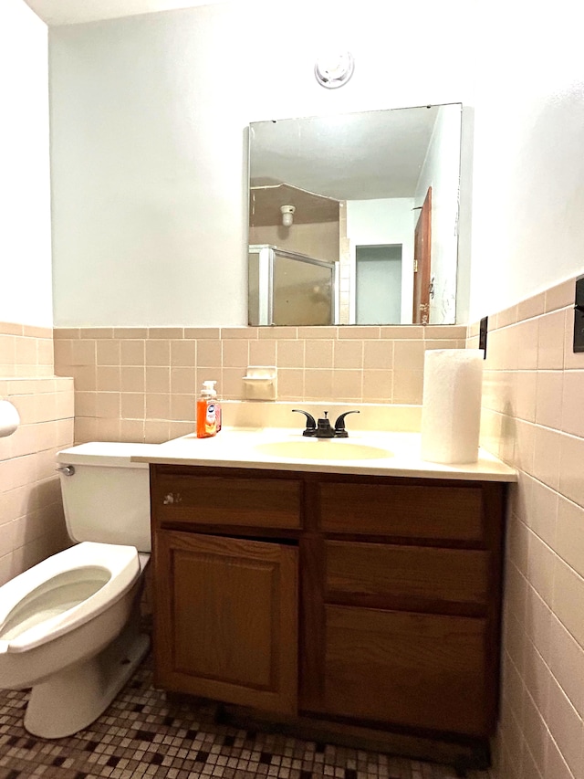 bathroom featuring vanity, toilet, a shower with door, and tile walls