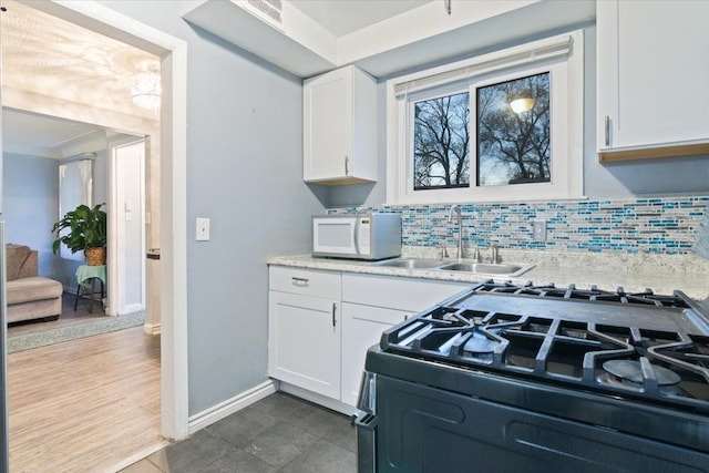 kitchen with decorative backsplash, white cabinetry, sink, and range with gas cooktop