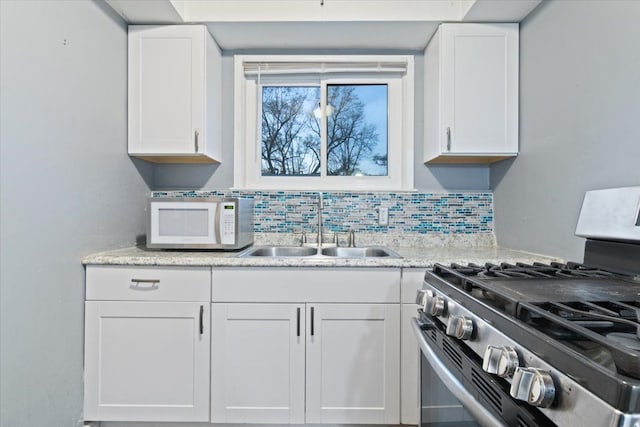 kitchen with backsplash, stainless steel gas range oven, white cabinetry, and sink