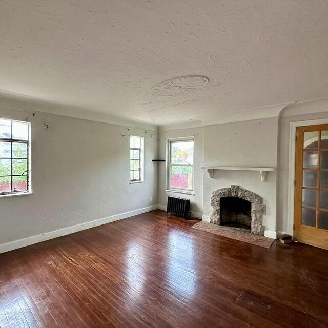 10728 Worden St, Detroit, MI 48224 - unfurnished living room featuring a textured ceiling, radiator, hardwood / wood-style flooring, baseboards, and a fireplace with flush hearth