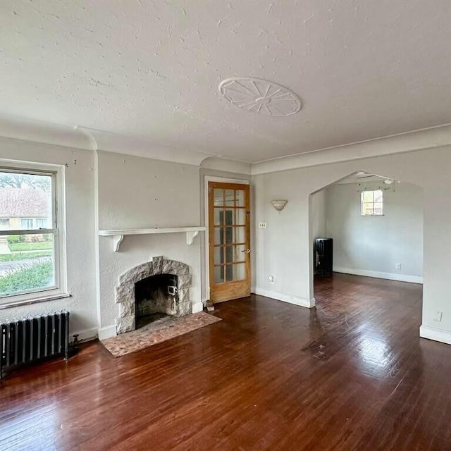 unfurnished living room featuring a textured ceiling, a stone fireplace, radiator heating unit, and dark wood-type flooring