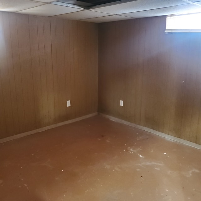 basement featuring wooden walls, a drop ceiling, and baseboards