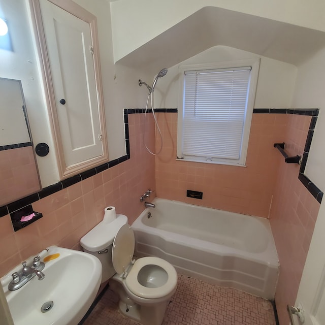 bathroom with tile patterned flooring, toilet, a sink, bathing tub / shower combination, and tile walls