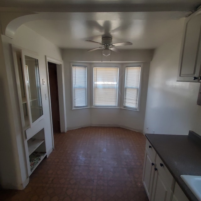 unfurnished dining area featuring arched walkways, dark floors, plenty of natural light, and a ceiling fan