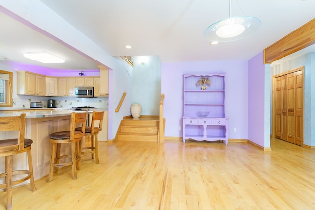 kitchen with decorative backsplash, light hardwood / wood-style floors, a breakfast bar area, and light brown cabinetry