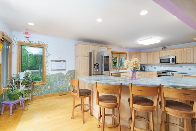 kitchen with a breakfast bar area, decorative backsplash, light brown cabinetry, light hardwood / wood-style floors, and stainless steel appliances