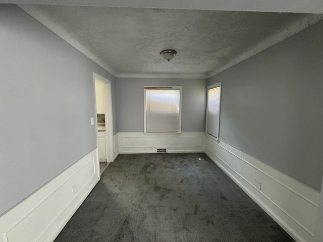 spare room featuring a textured ceiling and dark carpet