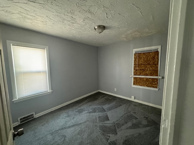 empty room featuring dark carpet and a textured ceiling