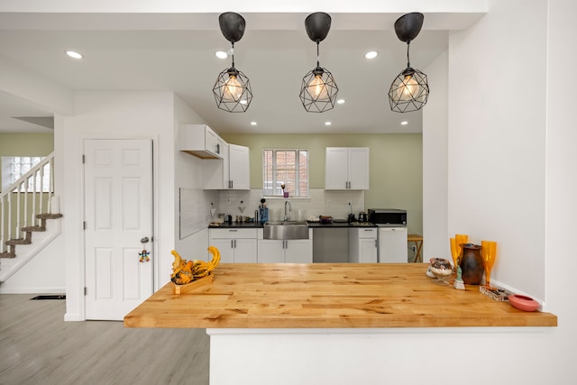 kitchen featuring backsplash, sink, pendant lighting, light hardwood / wood-style flooring, and white cabinets