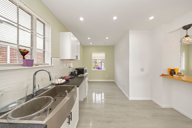 kitchen with light wood-type flooring, backsplash, sink, white cabinets, and hanging light fixtures