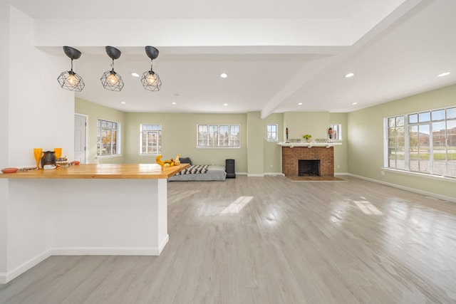 kitchen with hanging light fixtures, butcher block countertops, kitchen peninsula, a fireplace, and light wood-type flooring