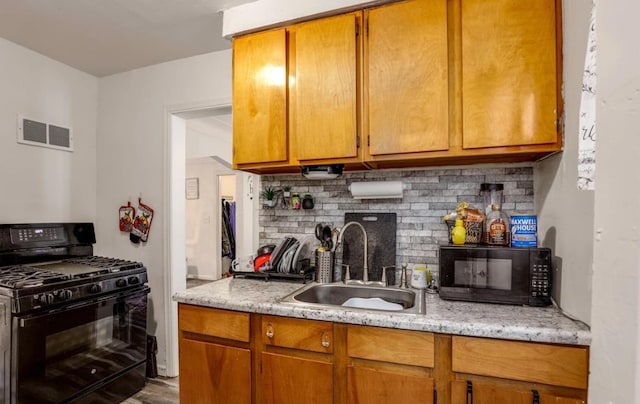 kitchen featuring sink, light stone counters, backsplash, wood-type flooring, and black appliances