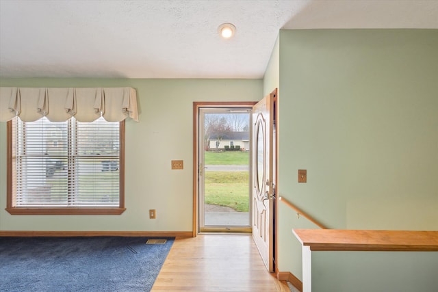 doorway to outside featuring light hardwood / wood-style flooring, a healthy amount of sunlight, and a textured ceiling