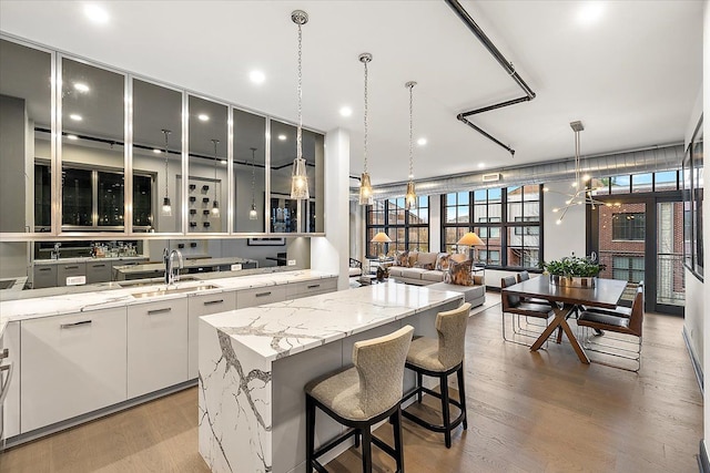 kitchen featuring light stone counters, sink, decorative light fixtures, white cabinets, and a kitchen island