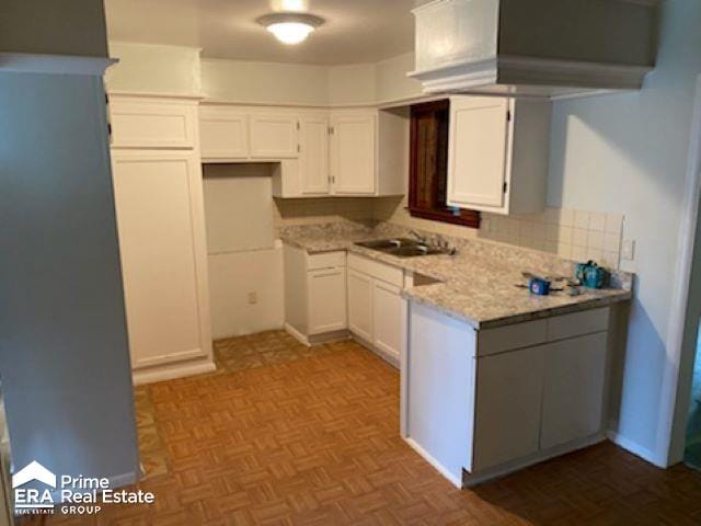 kitchen with white cabinets, light stone counters, parquet flooring, and sink