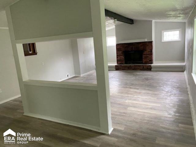 unfurnished living room featuring hardwood / wood-style floors, lofted ceiling with beams, and a brick fireplace