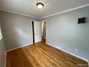 unfurnished bedroom featuring wood-type flooring and crown molding