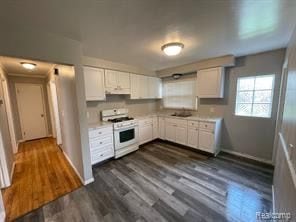 kitchen with white range, dark hardwood / wood-style floors, white cabinetry, and sink