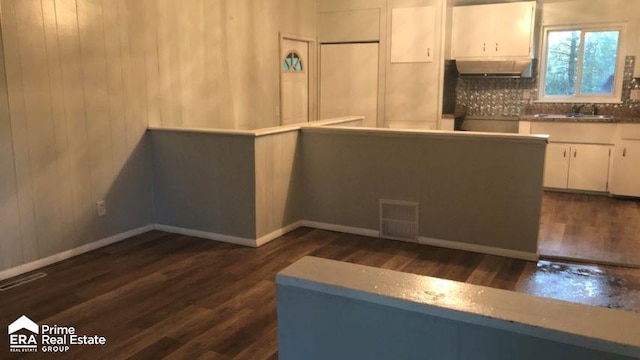 kitchen featuring backsplash, sink, wooden walls, dark hardwood / wood-style flooring, and white cabinetry