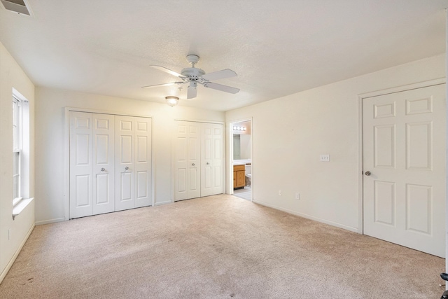 unfurnished bedroom with ensuite bath, ceiling fan, a textured ceiling, light colored carpet, and multiple closets