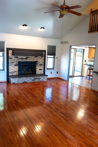 unfurnished living room with a brick fireplace, ceiling fan, high vaulted ceiling, and hardwood / wood-style flooring