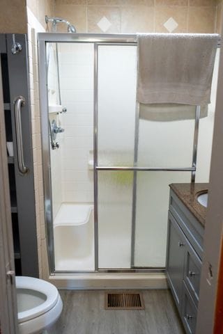 bathroom featuring toilet, vanity, an enclosed shower, and hardwood / wood-style flooring