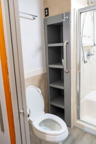 bathroom featuring hardwood / wood-style floors, toilet, walk in shower, and tile walls