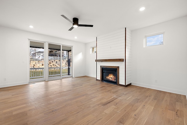 unfurnished living room with ceiling fan, a fireplace, and light wood-type flooring