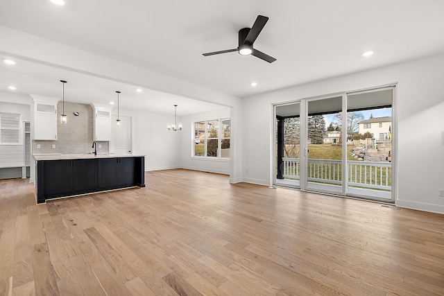 unfurnished living room featuring ceiling fan with notable chandelier and light hardwood / wood-style flooring