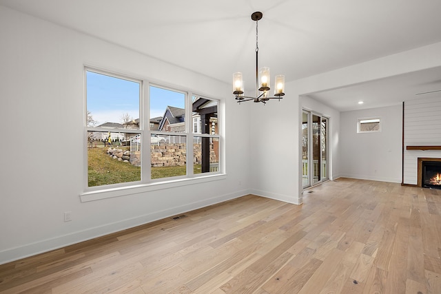 unfurnished dining area featuring a chandelier, a fireplace, and light hardwood / wood-style floors