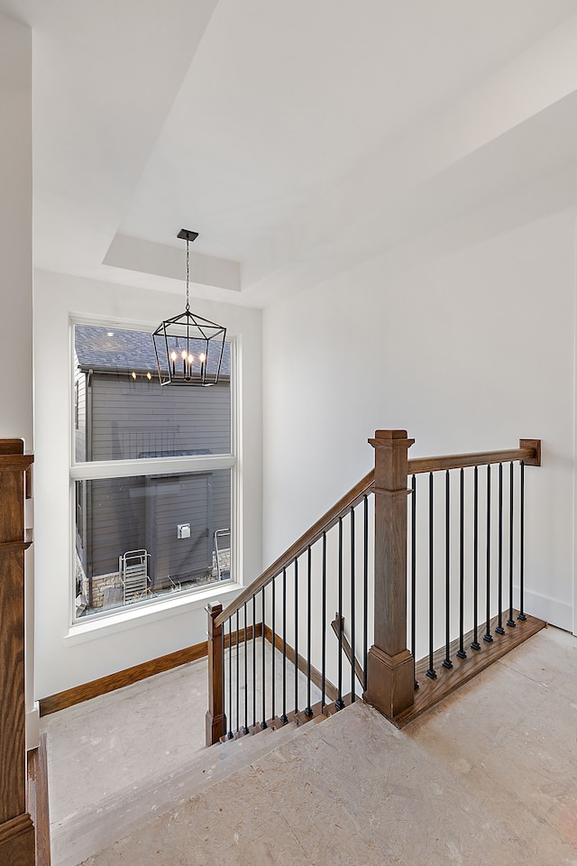 stairway with a raised ceiling and an inviting chandelier