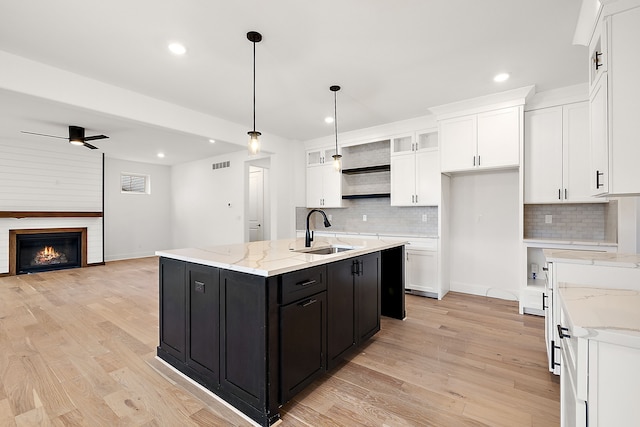 kitchen featuring pendant lighting, a kitchen island with sink, white cabinets, sink, and light hardwood / wood-style flooring