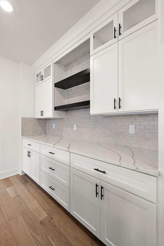 kitchen featuring light hardwood / wood-style floors, light stone counters, white cabinetry, and backsplash