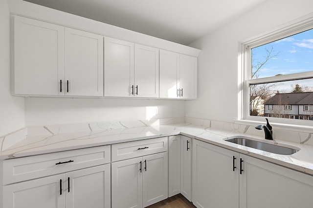 kitchen with white cabinets, light stone countertops, sink, and hardwood / wood-style flooring