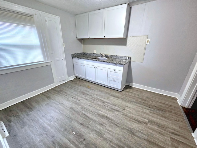 kitchen featuring white cabinetry, sink, dark stone counters, a textured ceiling, and light wood-type flooring