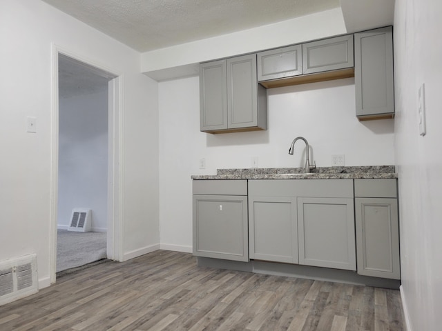 kitchen with light stone countertops, light wood-type flooring, gray cabinetry, a textured ceiling, and sink