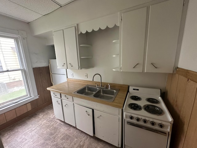 kitchen featuring a paneled ceiling, wood walls, white appliances, white cabinets, and sink