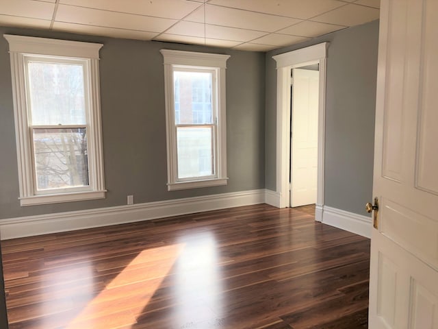 empty room with a paneled ceiling, plenty of natural light, and dark wood-type flooring