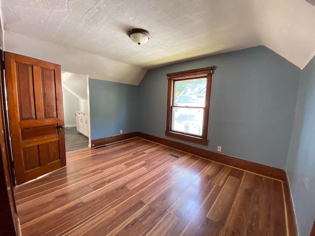 additional living space with hardwood / wood-style floors, a textured ceiling, and vaulted ceiling