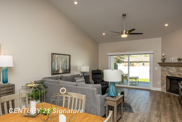 living room with ceiling fan, wood-type flooring, a stone fireplace, and high vaulted ceiling