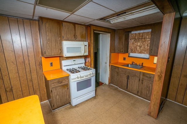 kitchen featuring white appliances, a drop ceiling, wood walls, and sink